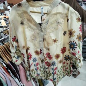 Women's cream-colored top with wildflower hem print and large white lace embroidery on the chest.