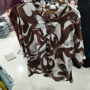 A person holding a brown and white abstract print V-neck blouse on a wooden hanger in a clothing store.