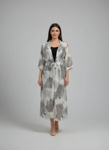 Woman wearing a white and grey botanical print long-sleeve duster with a belted waist and black top.