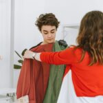 A mother assists her teenage son in selecting clothing in an indoor store setting.